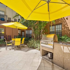 Grilling area and patio furniture both covered by yellow umbrellas in a calm courtyard at Visconti at Westshore