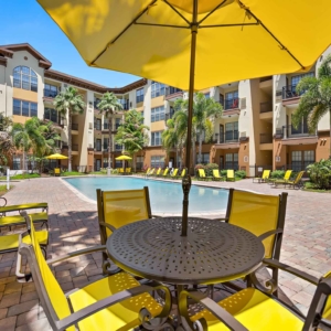 Yellow Patio umbrella with table and chairs overlooking Large Pool at Visconti with bright yellow patio furniture and buildings of Visconti at Westshore surrounding