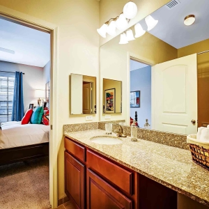 Large bathroom with single sink granite counter looking into bedroom with large windows